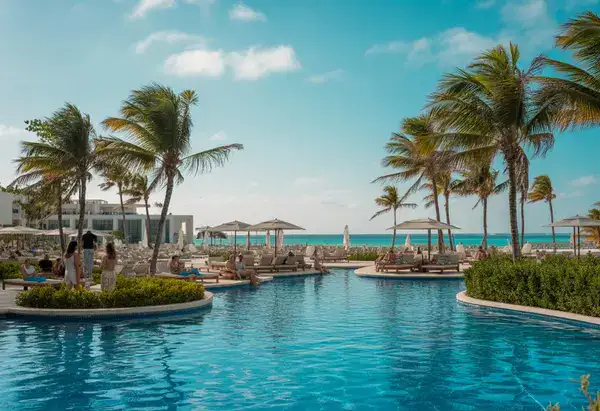 Beachfront resort with white buildings, palm trees, an infinity pool by the ocean.